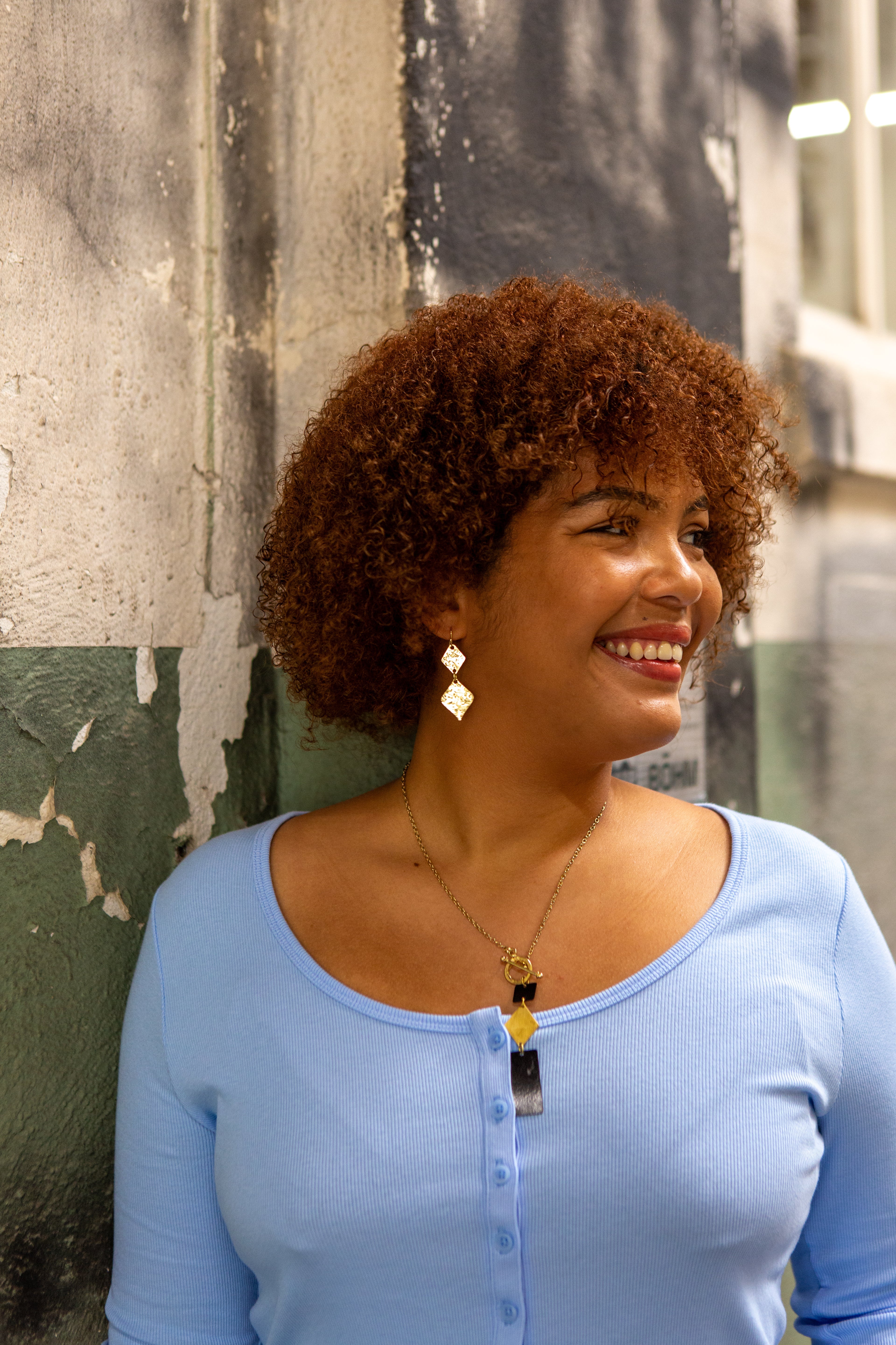 Gold-plated hammered rhombus dangle earrings on a slate background