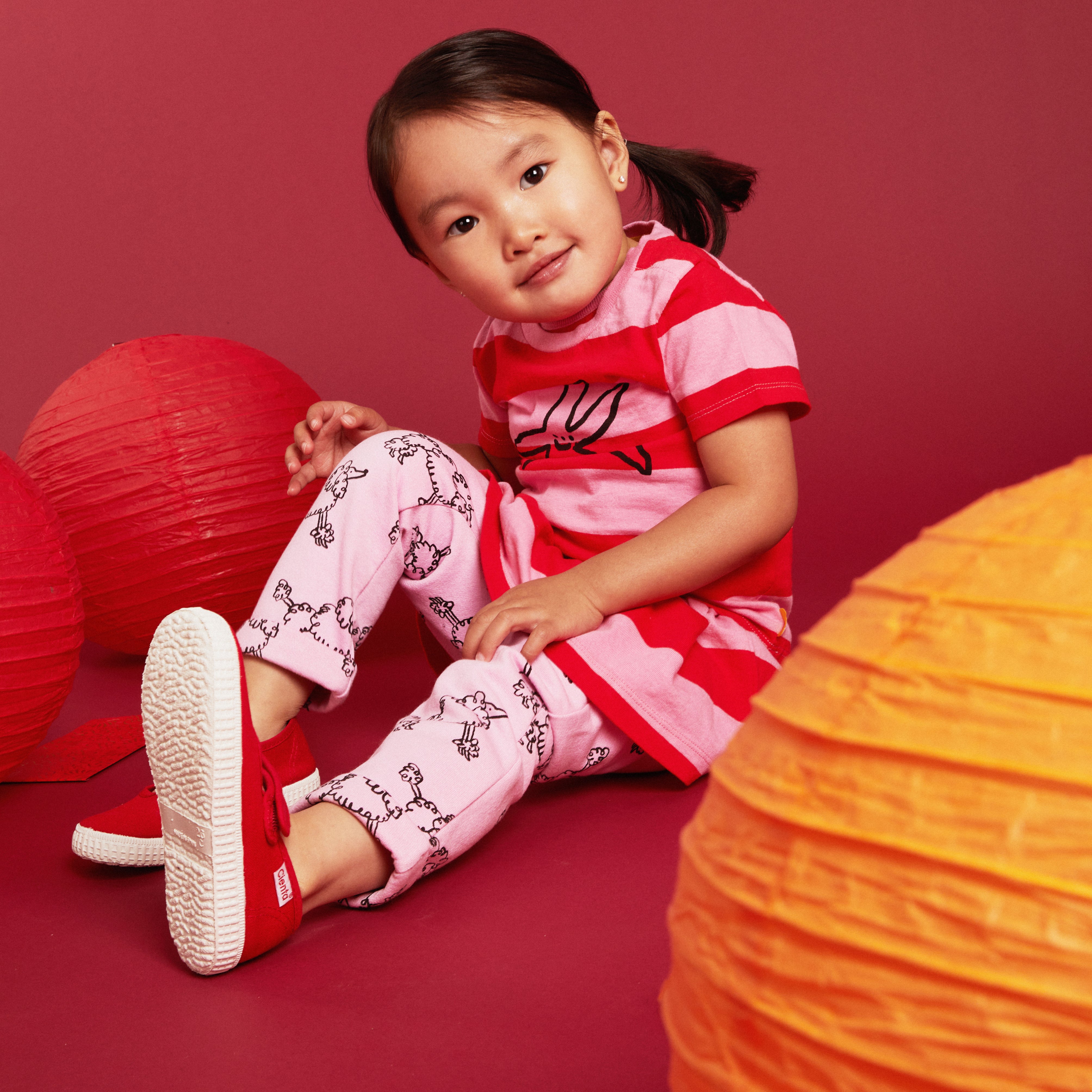 Child in red and pink outfit with paper lanterns on a red background