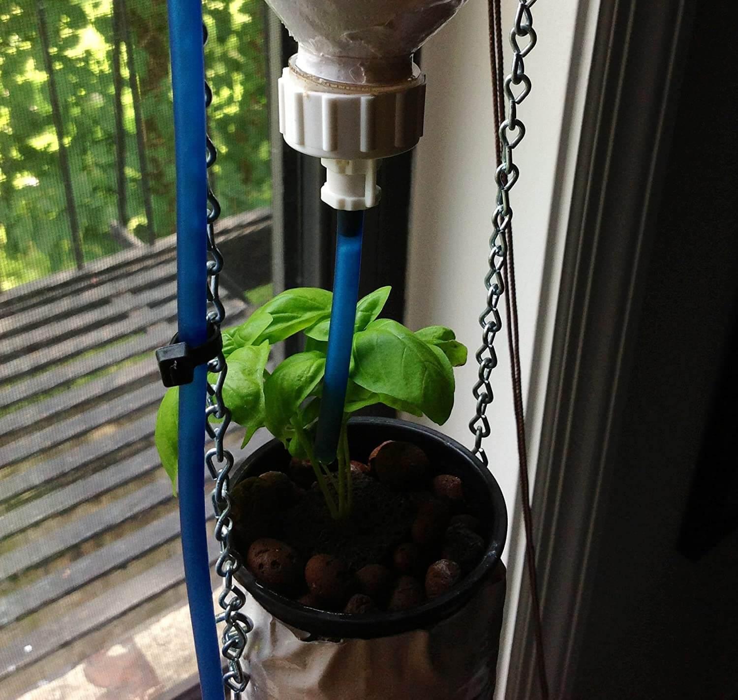 Potted plant hanging from a blue stand with a water source above it, on a balcony.
