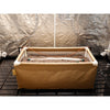 Rectangular grow box with soil and irrigation system inside, against a reflective wall.
