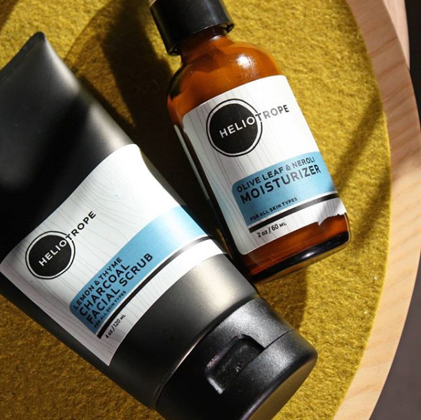 Heliotrope SF Olive Leaf and Neroli Moisturizer alongside a natural botanical scrub on a yellow background