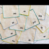 Set of 8 sweary cocktail coasters laid out flat, each showing a different letter representing a swear word, made from linen and poly blend