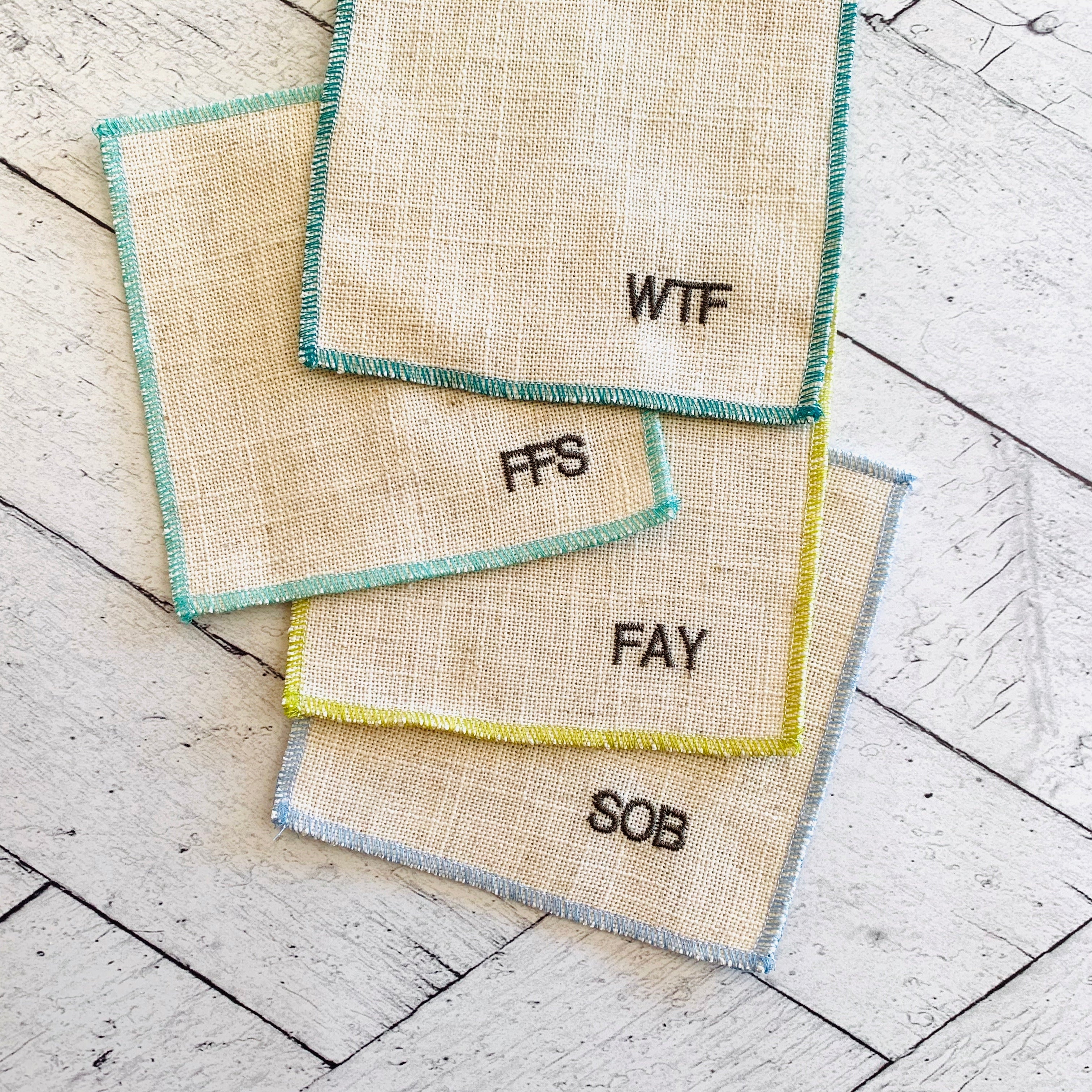 Sweary cocktail coasters styled on a bar cart with drinks, showing the full set of 8 funny linen coasters