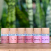 Set of small cylindrical containers with cork lids on a wooden surface, against a blurred green plant background.