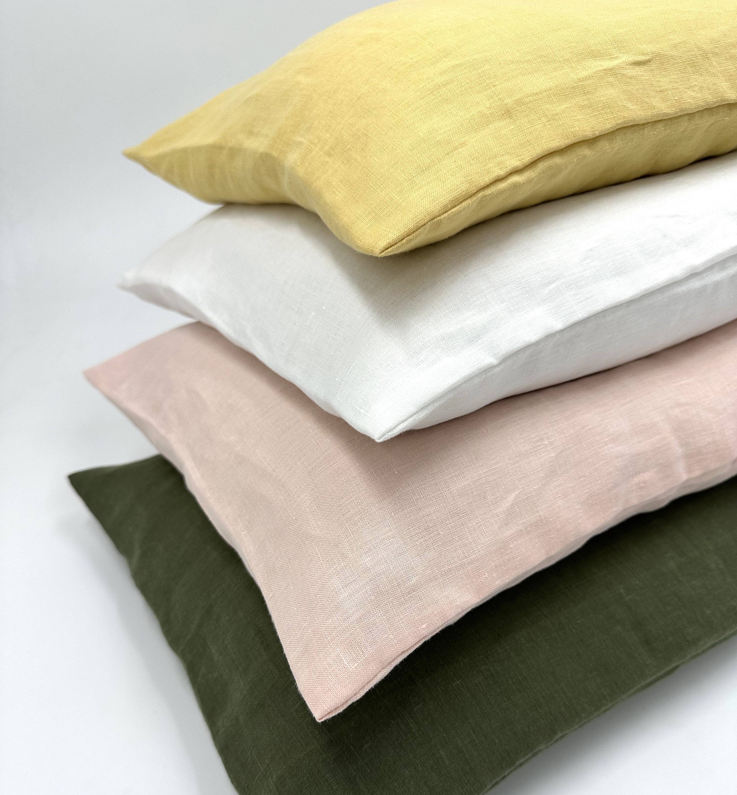 Stack of four linen pillows in yellow, white, pink, and green on a light gray background.