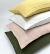 Stack of four linen pillows in yellow, white, pink, and green on a light gray background.