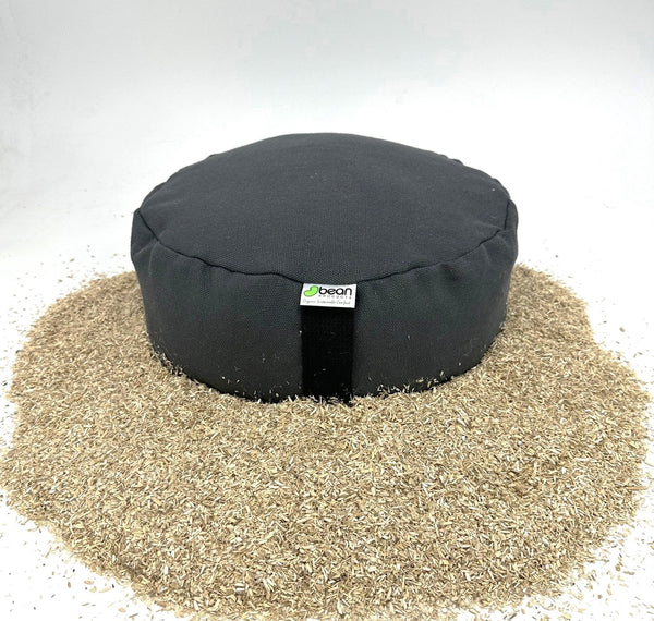 Black meditation pillow on a bed of sand with a white background