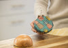 Person holding a pineapple-patterned food storage container on a wooden cutting board with an onion.