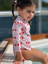 Young girl in a cherry-patterned swimsuit sitting by a pool.