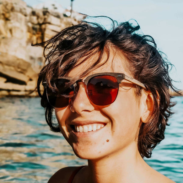 Person wearing sunglasses with a scenic background of water and rocks