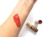 Red lipstick on a person's arm with a tube of lipstick next to it on a white background