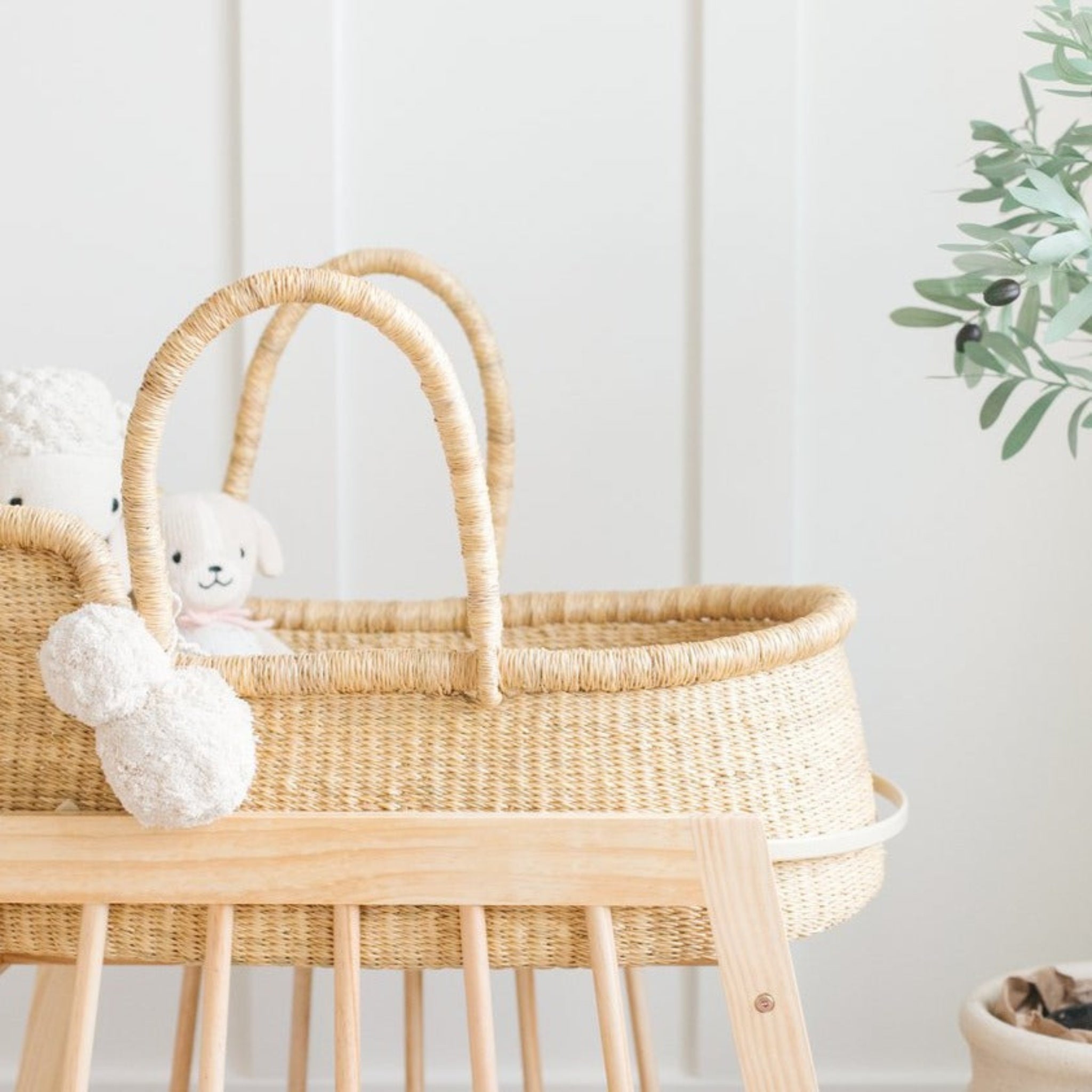Wicker baby Moses basket with plush toy against a white wall