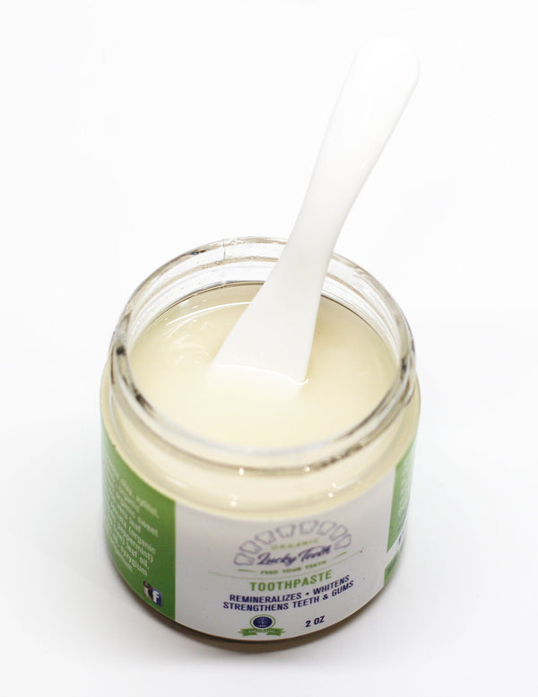 Jar of toothpaste with a white applicator on a white background