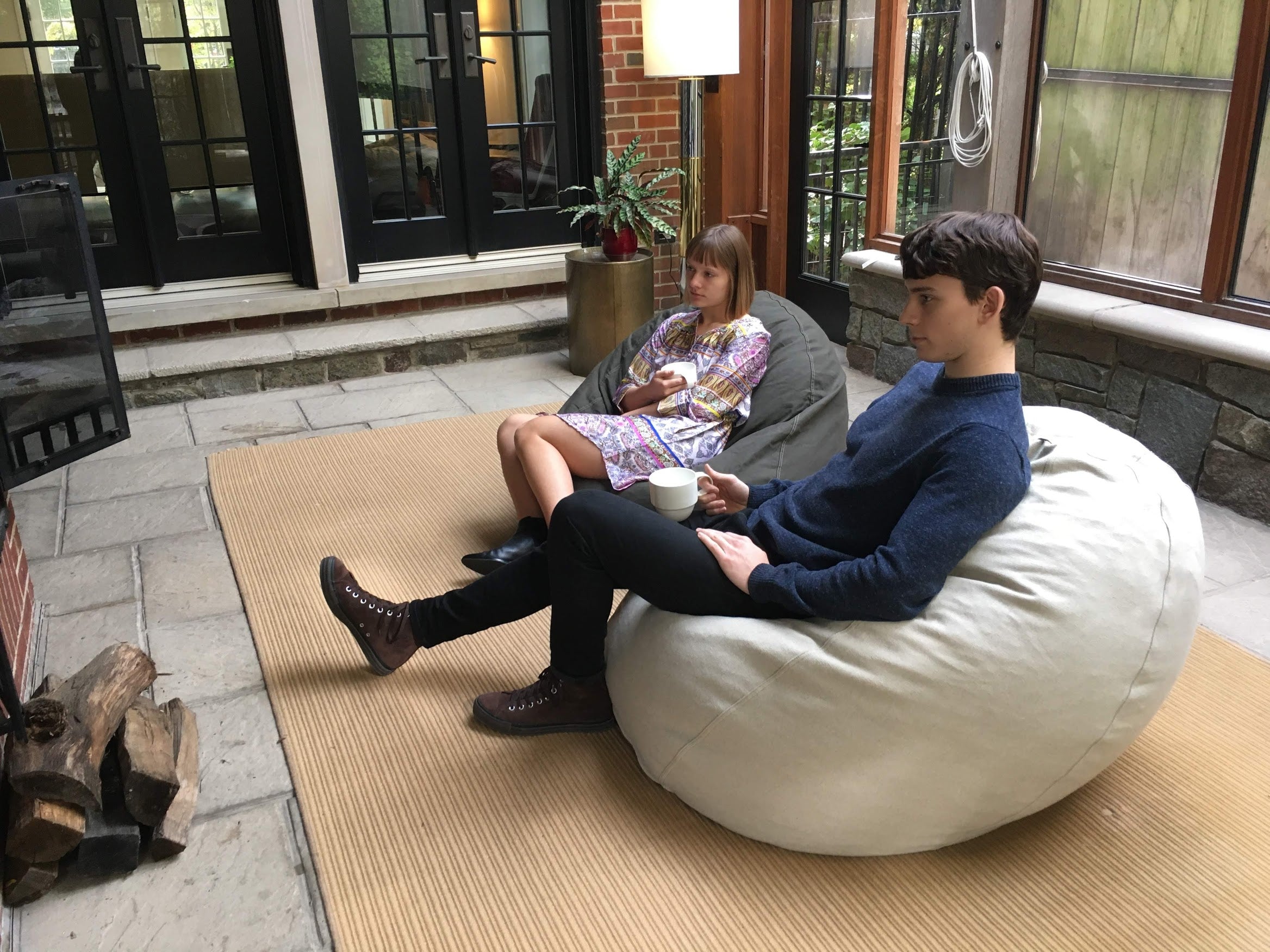 Two children sitting on bean bags in a patio area with a lamp and rug.