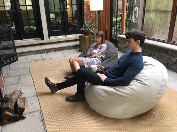 Two children sitting on bean bags in a patio area with a lamp and rug.