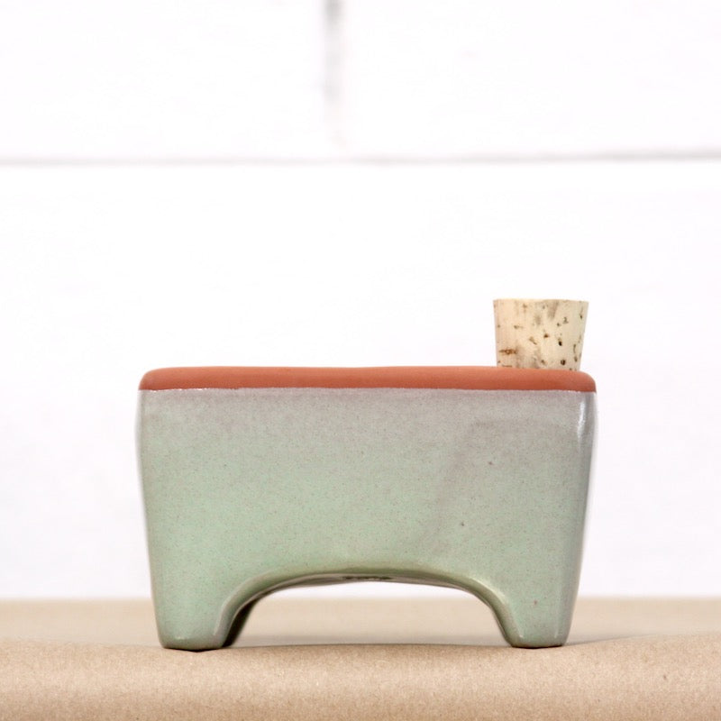 Ceramic planter with a textured surface and cork lid on a neutral background