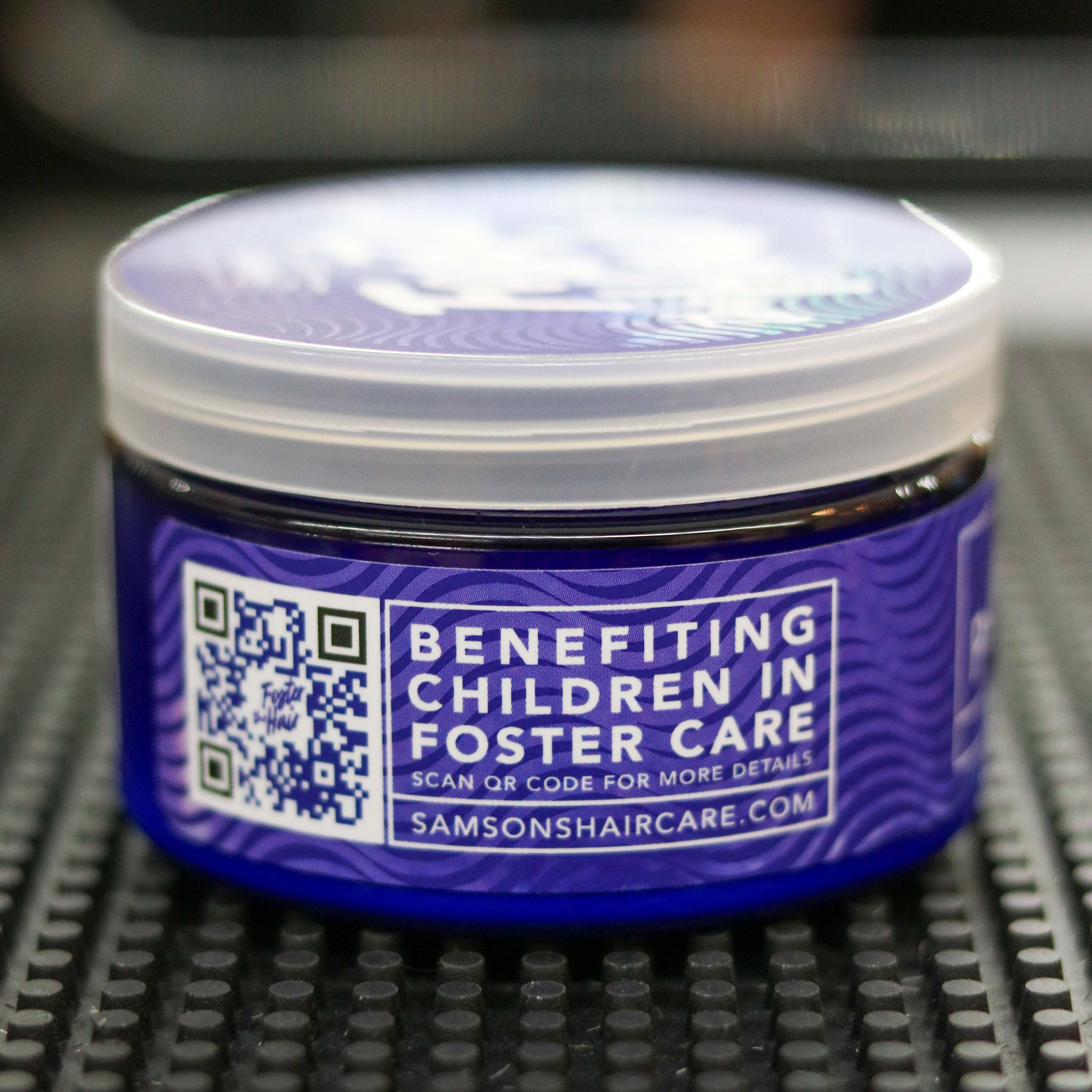 Blue container with a lid on a textured surface, featuring text about benefiting children in foster care.