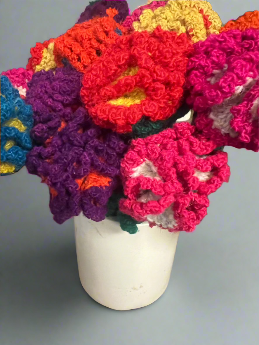 Colorful crocheted flowers in a white vase on a gray background