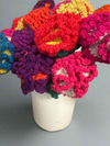 Colorful crocheted flowers in a white vase on a gray background