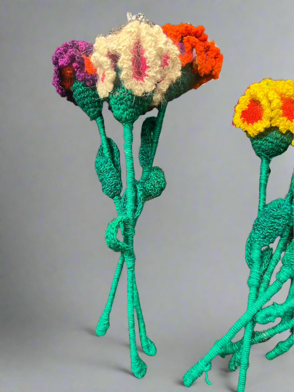 Colorful knitted flowers on green stems against a gray background
