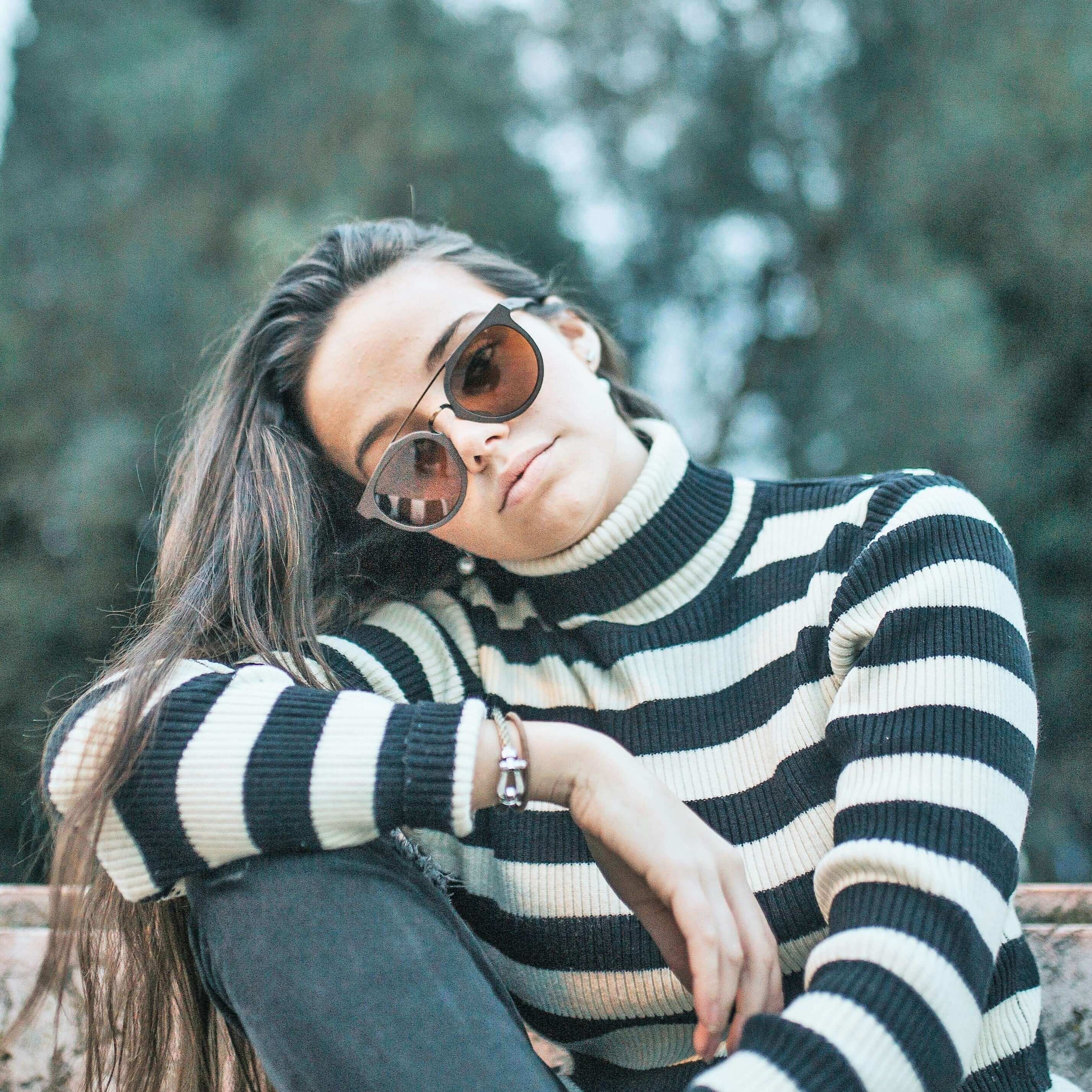 Woman wearing a black and white striped sweater with sunglasses, sitting outdoors.