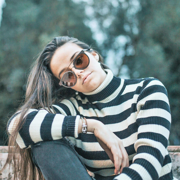 Woman wearing a black and white striped sweater with sunglasses, sitting outdoors.