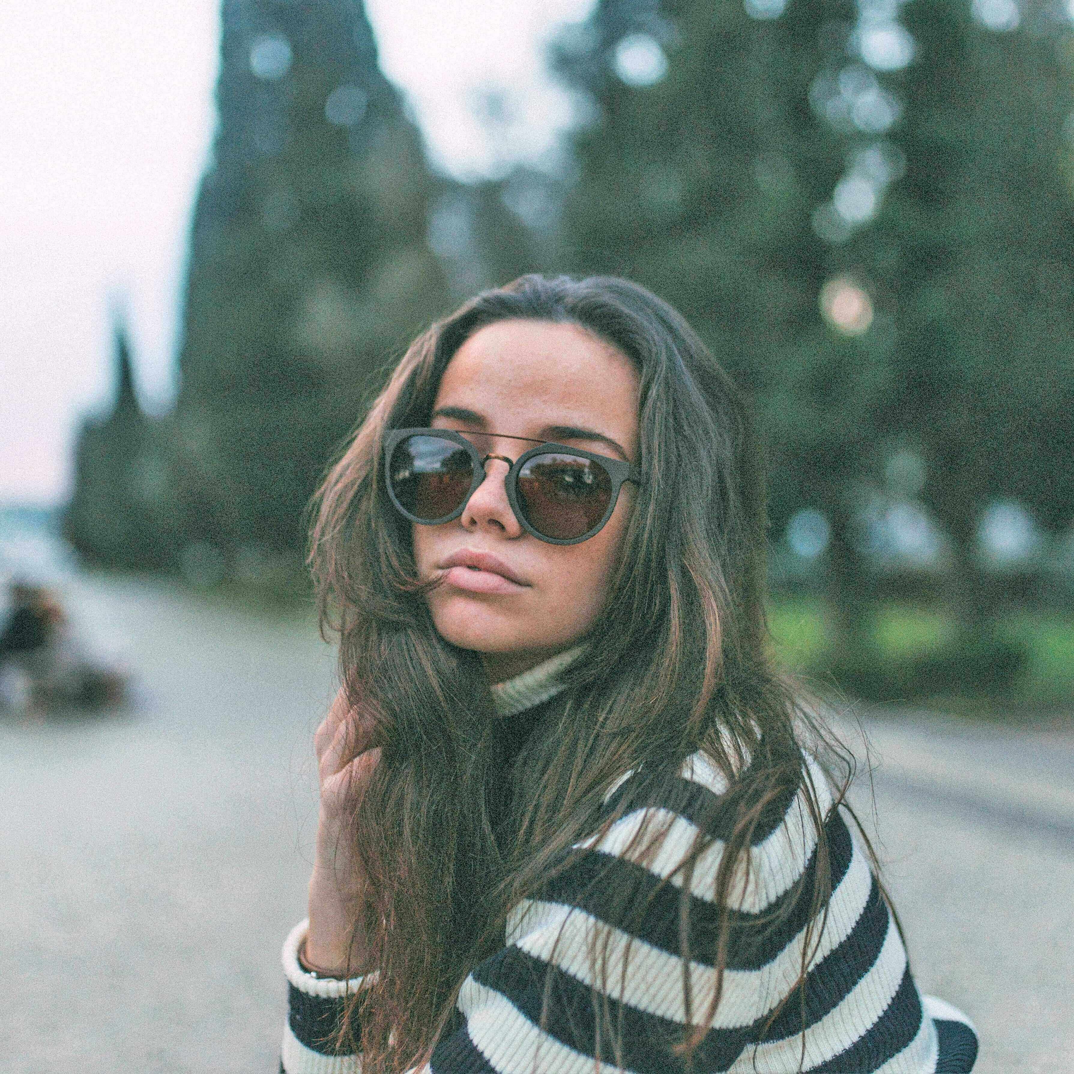 Woman wearing sunglasses and a striped sweater outdoors with trees in the background