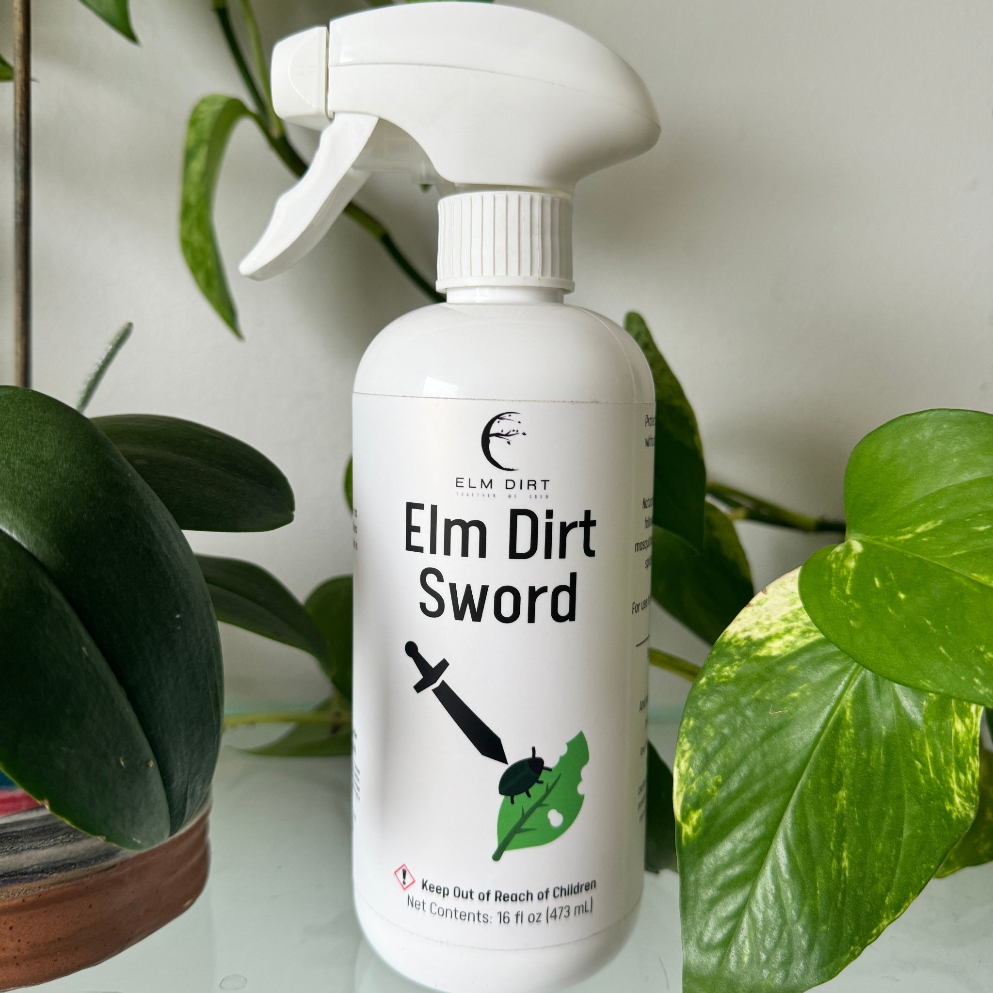 White spray bottle labeled 'Elm Dirt Sword' with green leaves in the background