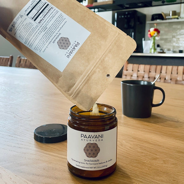 Paavani Ayurveda product being poured from a brown paper bag into a jar on a wooden table.