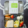 Metal lunchbox with compartments filled with food and an eco-safe label on a patterned background