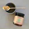 Jar of Paavani Ayurveda Vata Spice Blend with a spoonful of spice over a cup on a gray surface