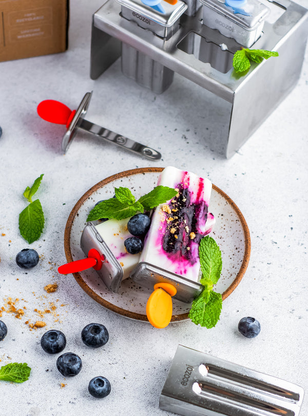 Ice cream maker with ice cream on a plate surrounded by berries and mint leaves on a light surface.