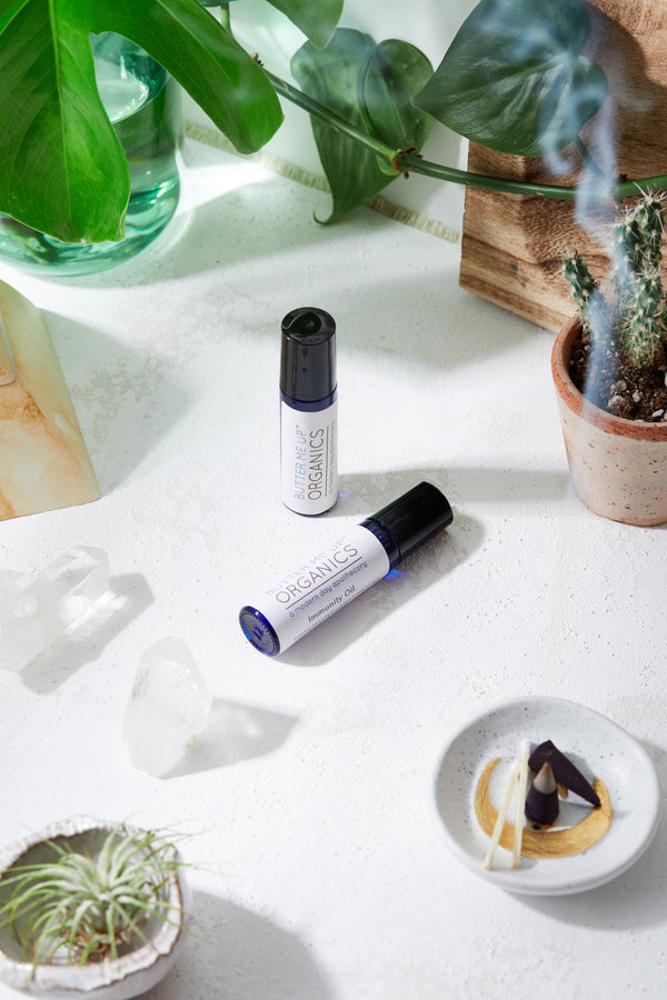 Two small bottles labeled 'ORGANICS' on a white surface with plants and a candle.