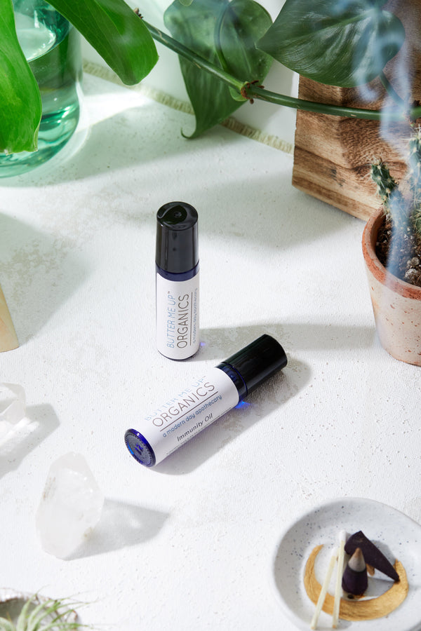 Two organic skincare products on a white surface with plants in the background