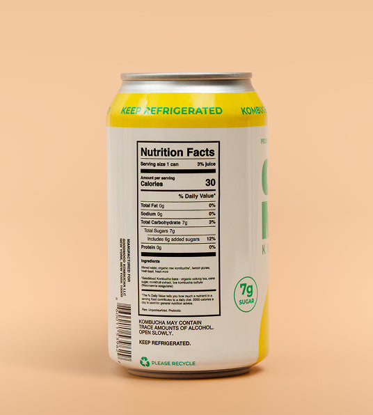 A 12 oz aluminum can of Kombucha with a white label, yellow accents, and a silver top, shown from the back with the Nutrition Facts label visible against a solid peach background.