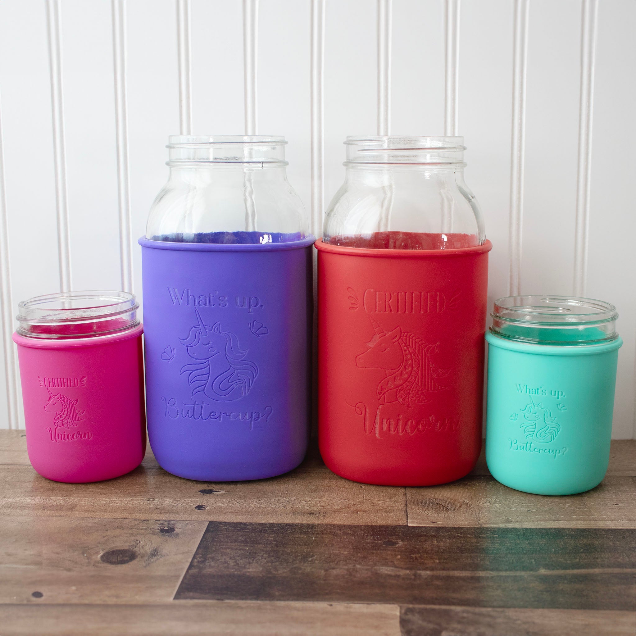 Five glass jars with colorful silicone sleeves on a wooden surface.
