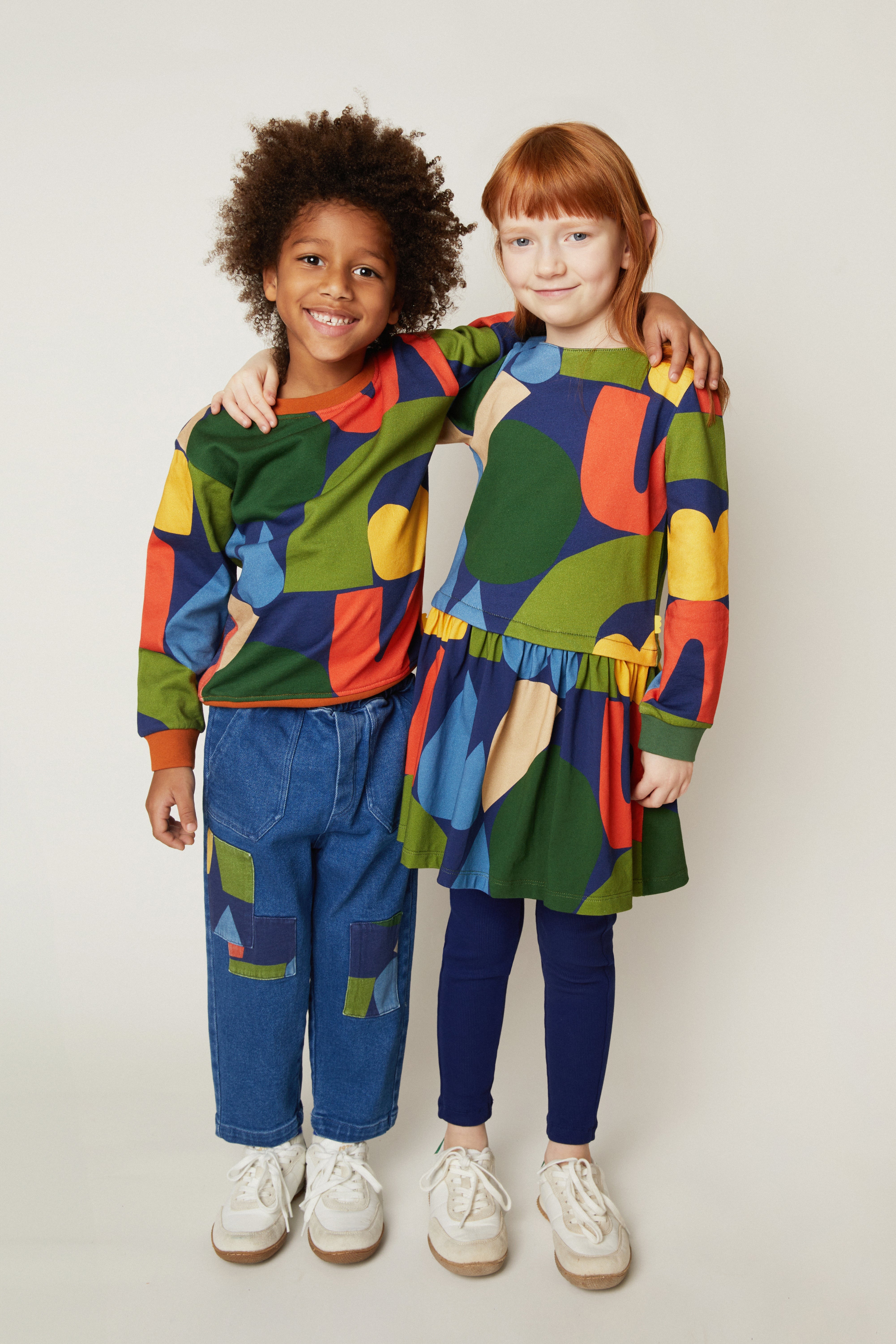 Two children wearing colorful outfits standing against a plain background