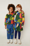 Two children wearing colorful outfits standing against a plain background