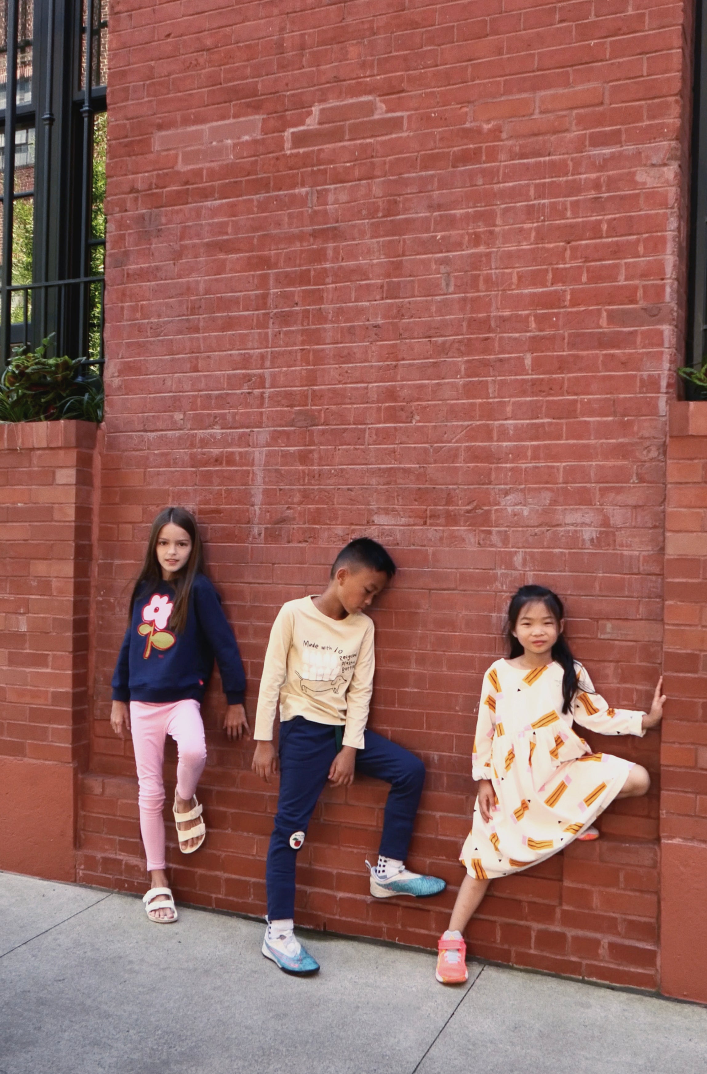 Three children posing against a red brick wall.