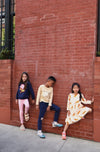 Three children posing against a red brick wall.