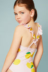 Young girl wearing a pink swimsuit with lemon print and ruffled straps against a light blue background