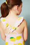 Back view of a child wearing a pink dress with lemon print against a light blue background