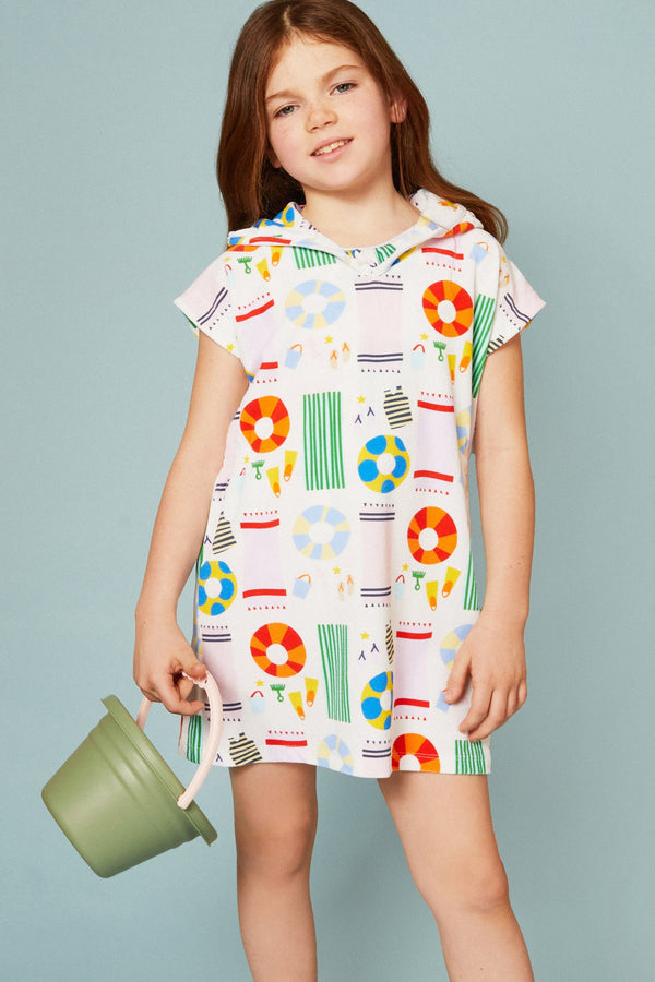 Young girl wearing a colorful patterned dress holding a green bucket against a light blue background