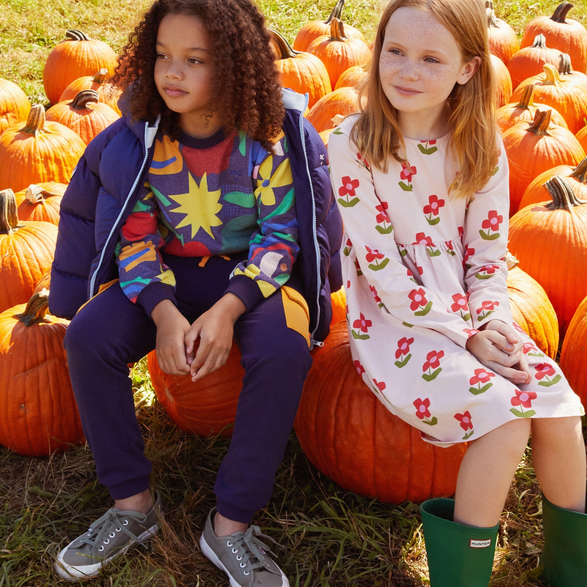 Two children sitting on pumpkins in a pumpkin patch