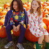 Two children sitting on pumpkins in a pumpkin patch