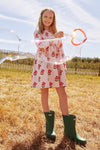 Young girl in a floral dress and green wellies standing in a field with bubbles.