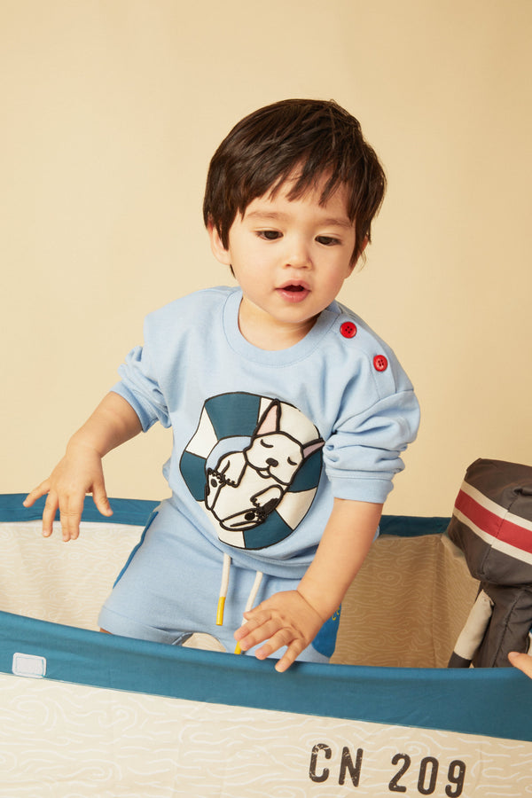 Child wearing a light blue outfit with a dog graphic, standing next to a suitcase.