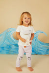 Child wearing a white t-shirt and light-colored pants with a starfish design, holding a starfish in front of a blue wave painting.