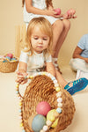 Child playing with a basket of Easter eggs on a beige background