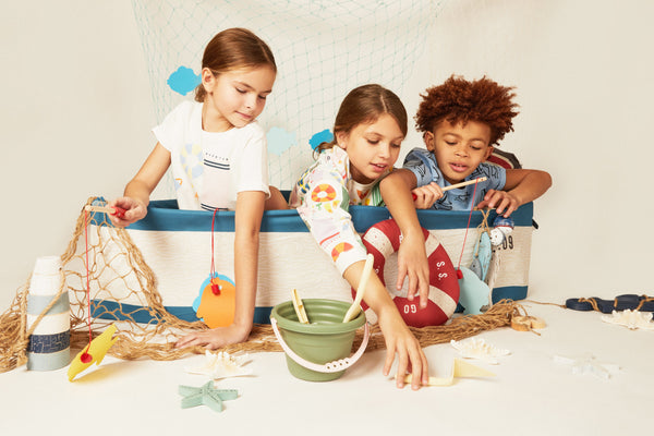 Three children playing with beach toys in a boat-like structure.